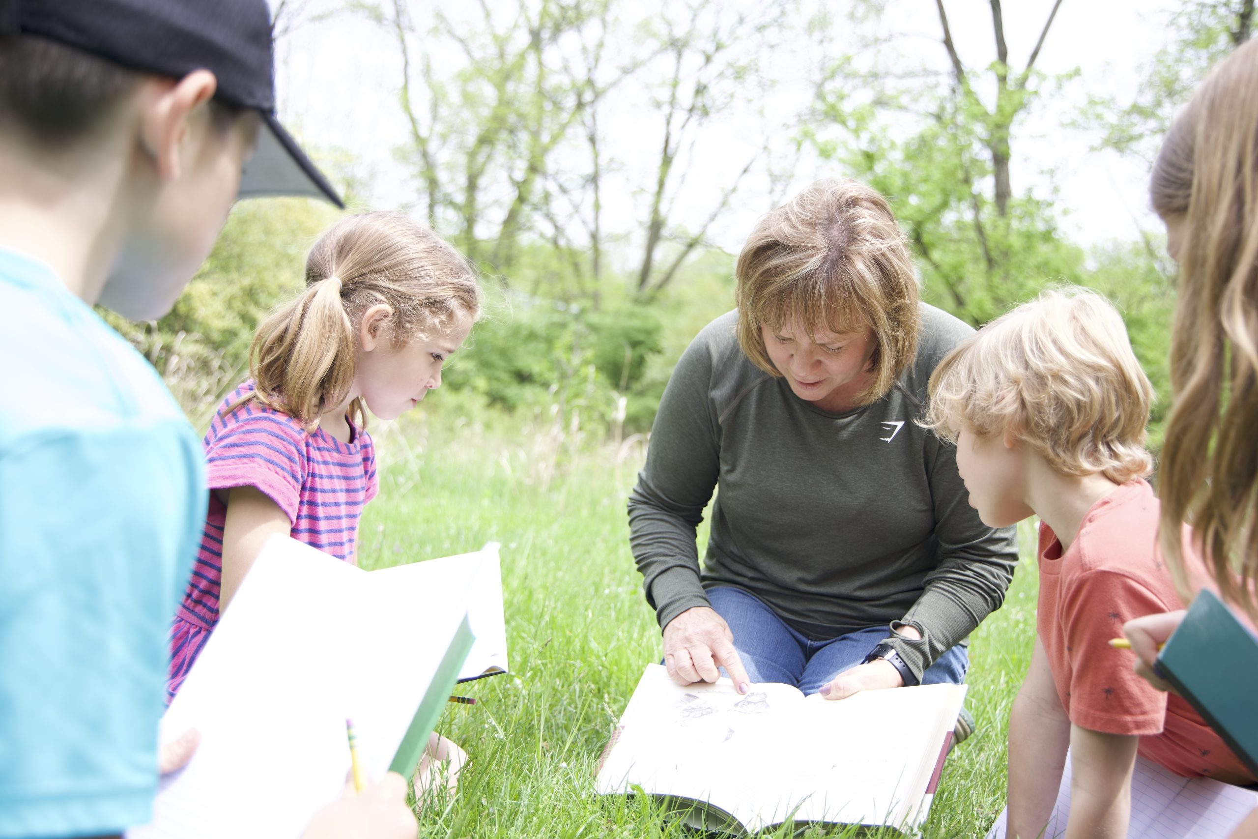 a woman and kids sitting in grass reading BOLDer Magazine